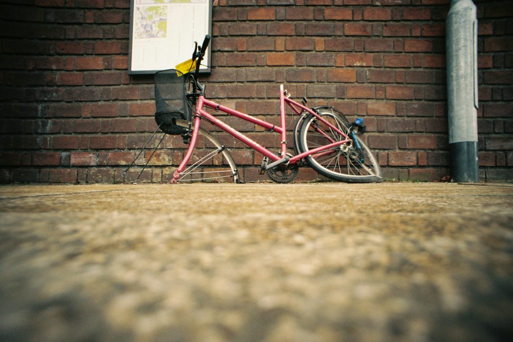 A pink bicycle lies on its side on a cobblestone street against a red brick wall. | Bike Accident Claims